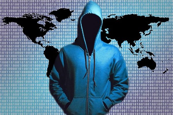 Image of hacker in hoodie with no face standing in front of a world map with 1s and 0s.